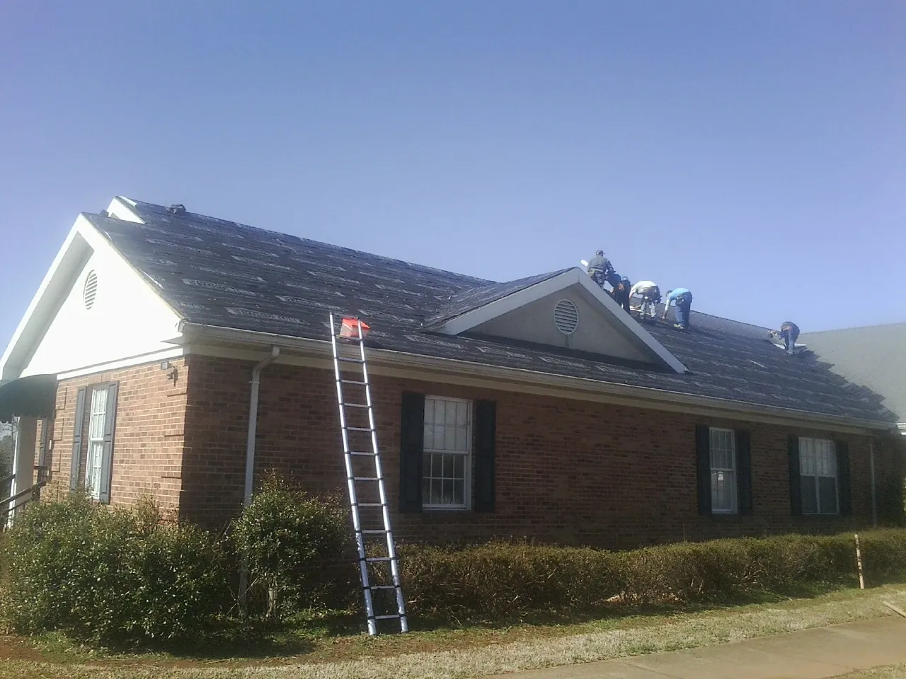 Crew tearing shingles off a brick ranch roof with a ladder set — Emergency Roof Repair work by our crew in Temperance