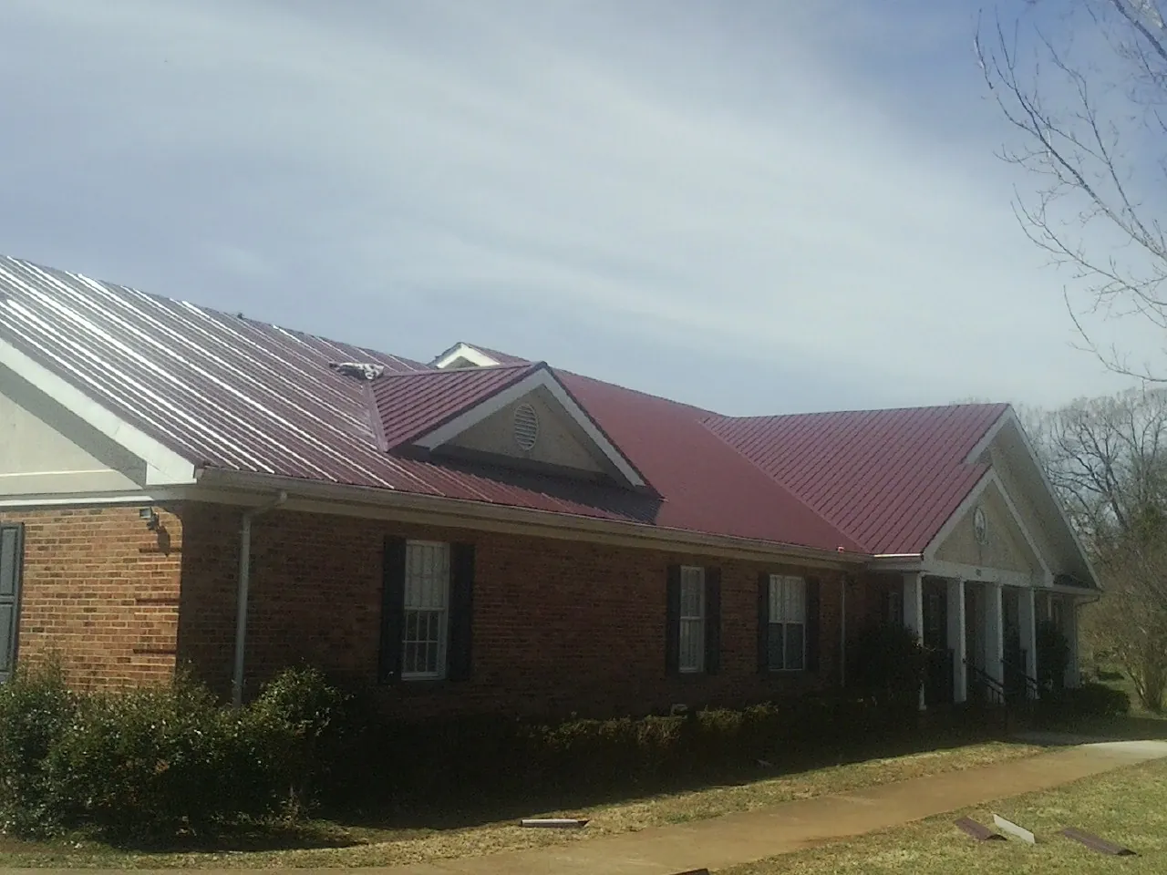 Red metal roof with gabled entries on a long brick building, from a Hail Damage Roof Repair job in Temperance