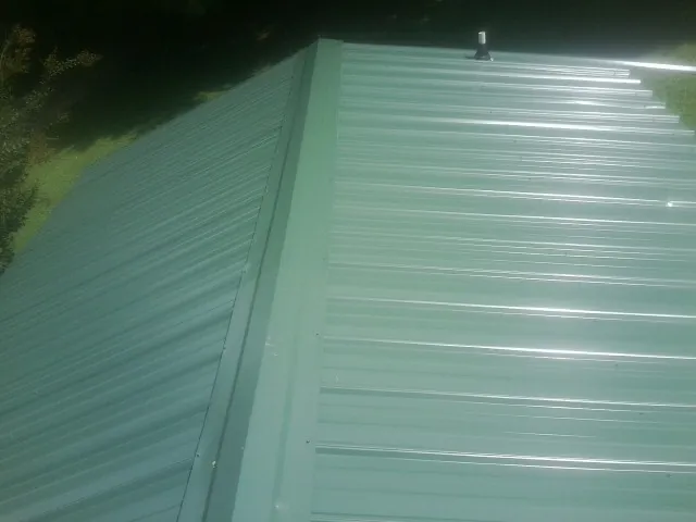 New green metal panels meeting at the ridge of a roof — Flat Roof Repair work by our crew in Temperance