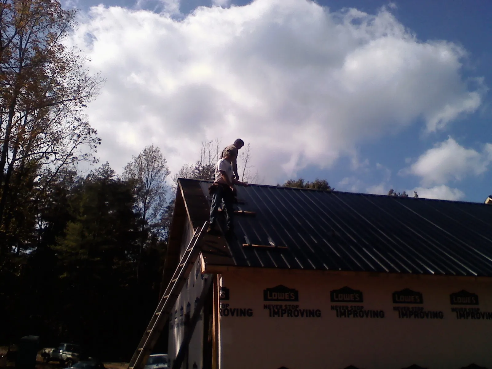Roofer fastening dark metal panels high against a cloudy sky, from a Roof Inspection job in Temperance