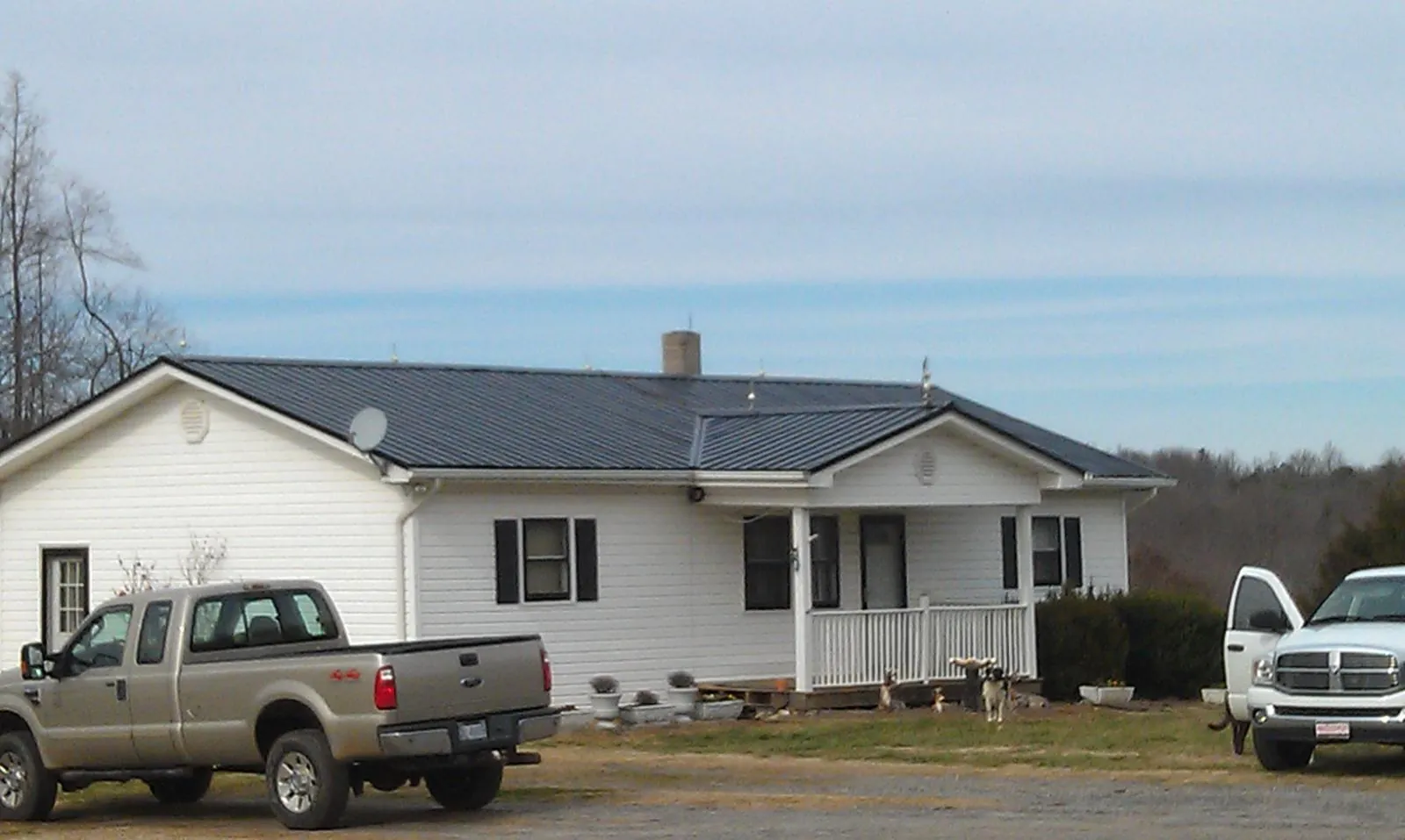 Finished dark metal roof on a white ranch home with work trucks parked in Temperance