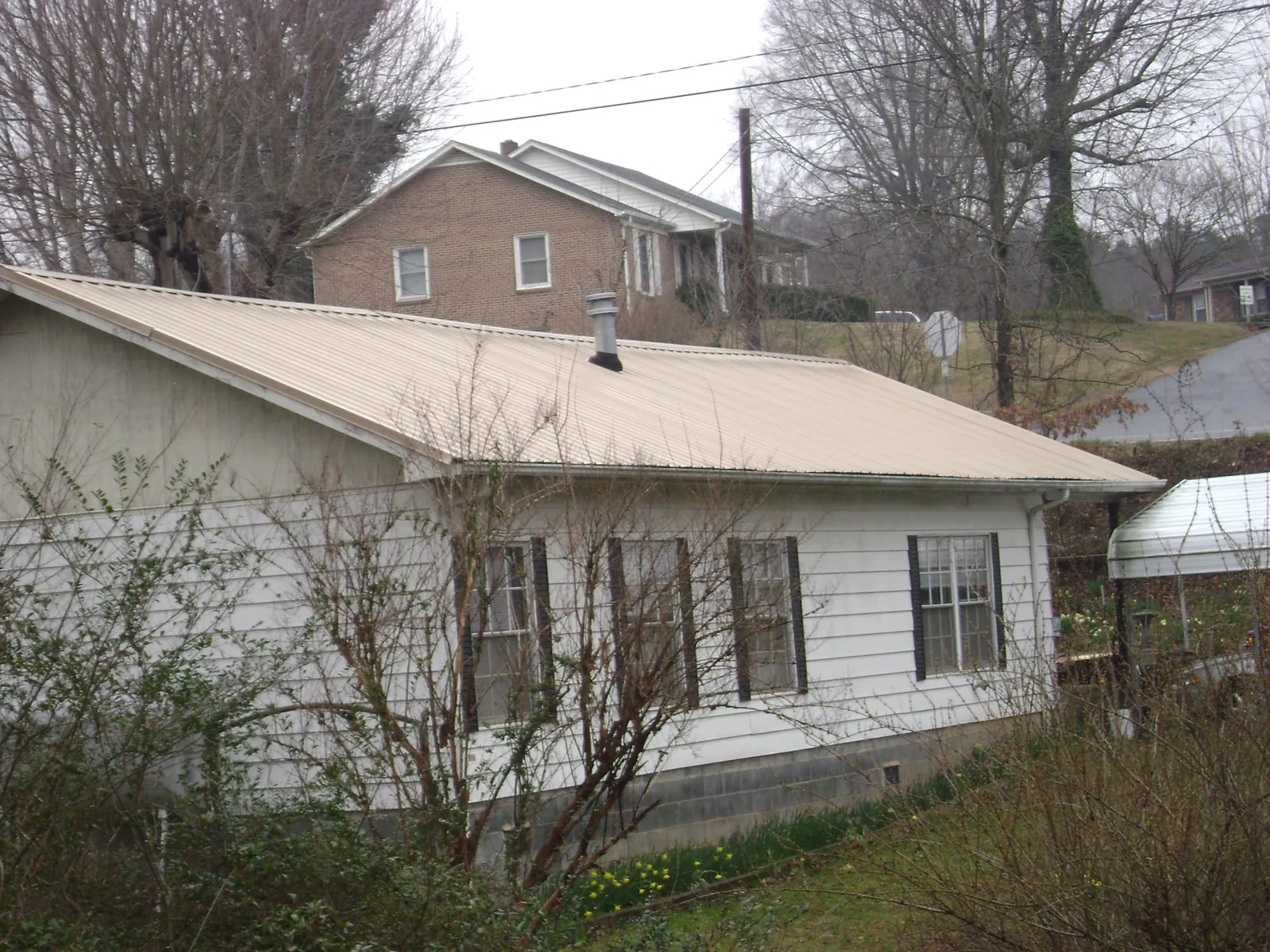 Tan metal roof on a white sided house set into a hillside — Commercial Roofing by Roofing Brothers in Temperance